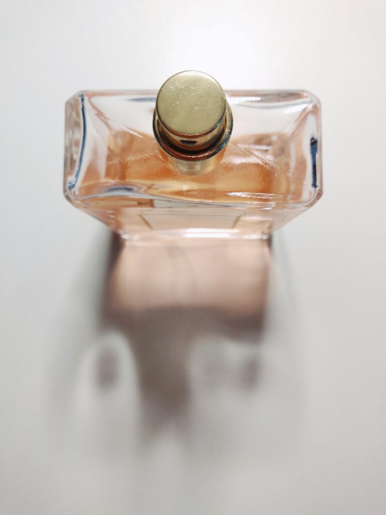 A close-up shot of an elegant perfume bottle with a golden cap on a white surface casting a shadow.